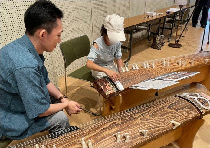 箏奏者の指導を受けながら演奏体験をする来場者