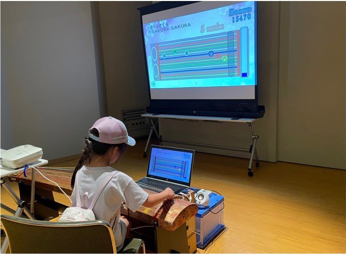 スクリーンを見ながらリズムゲーム「ことの名人」に挑戦する子ども