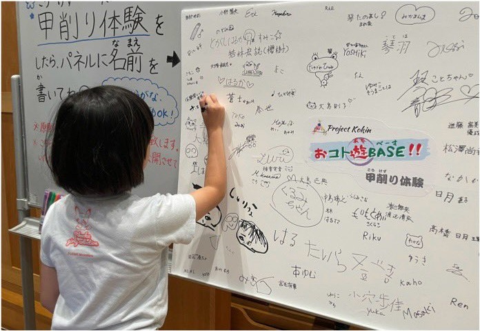 甲削り体験の記念にパネルへ名前を書く子ども